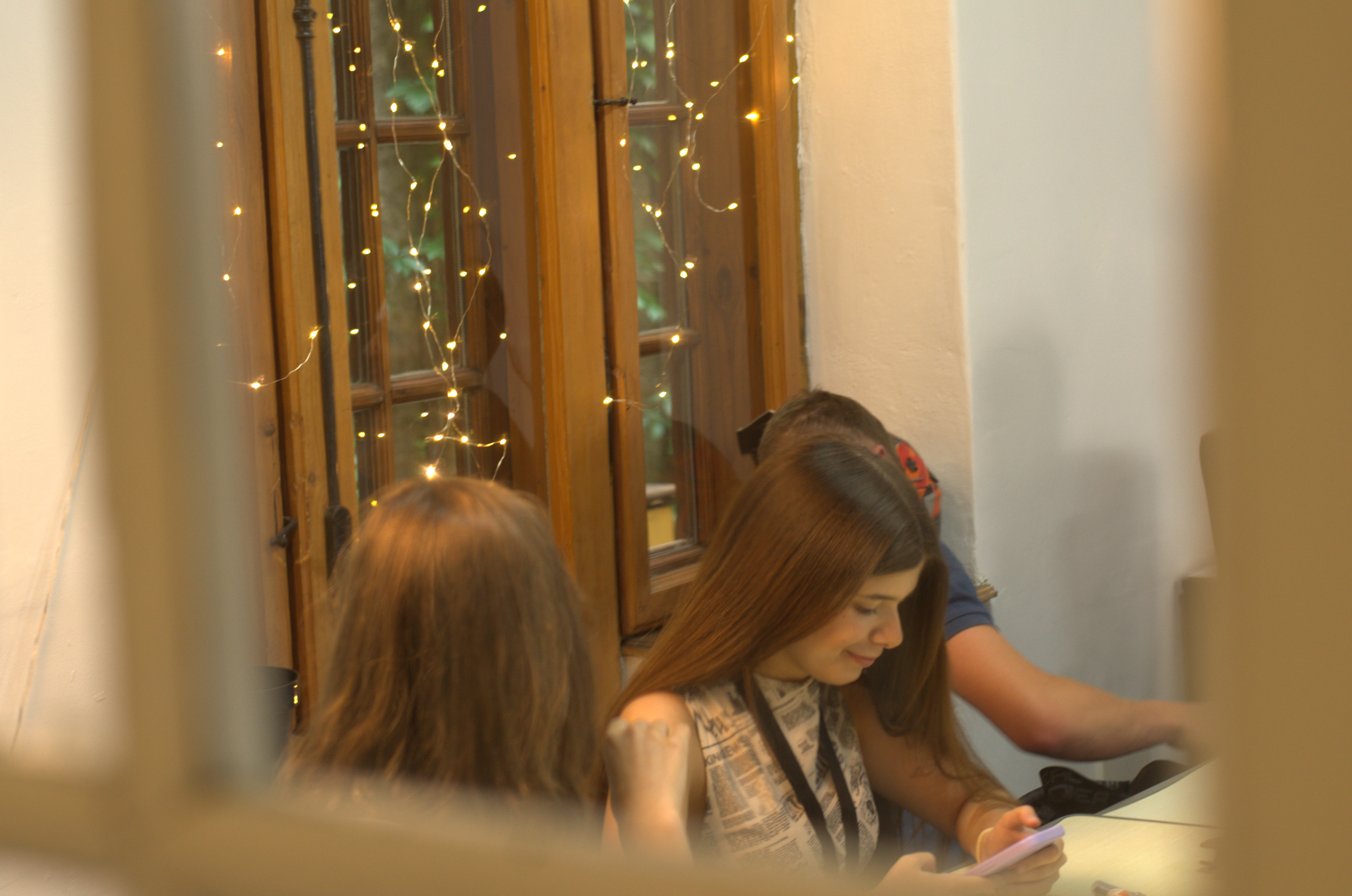 Students working at a table by a window decorated with fairy lights