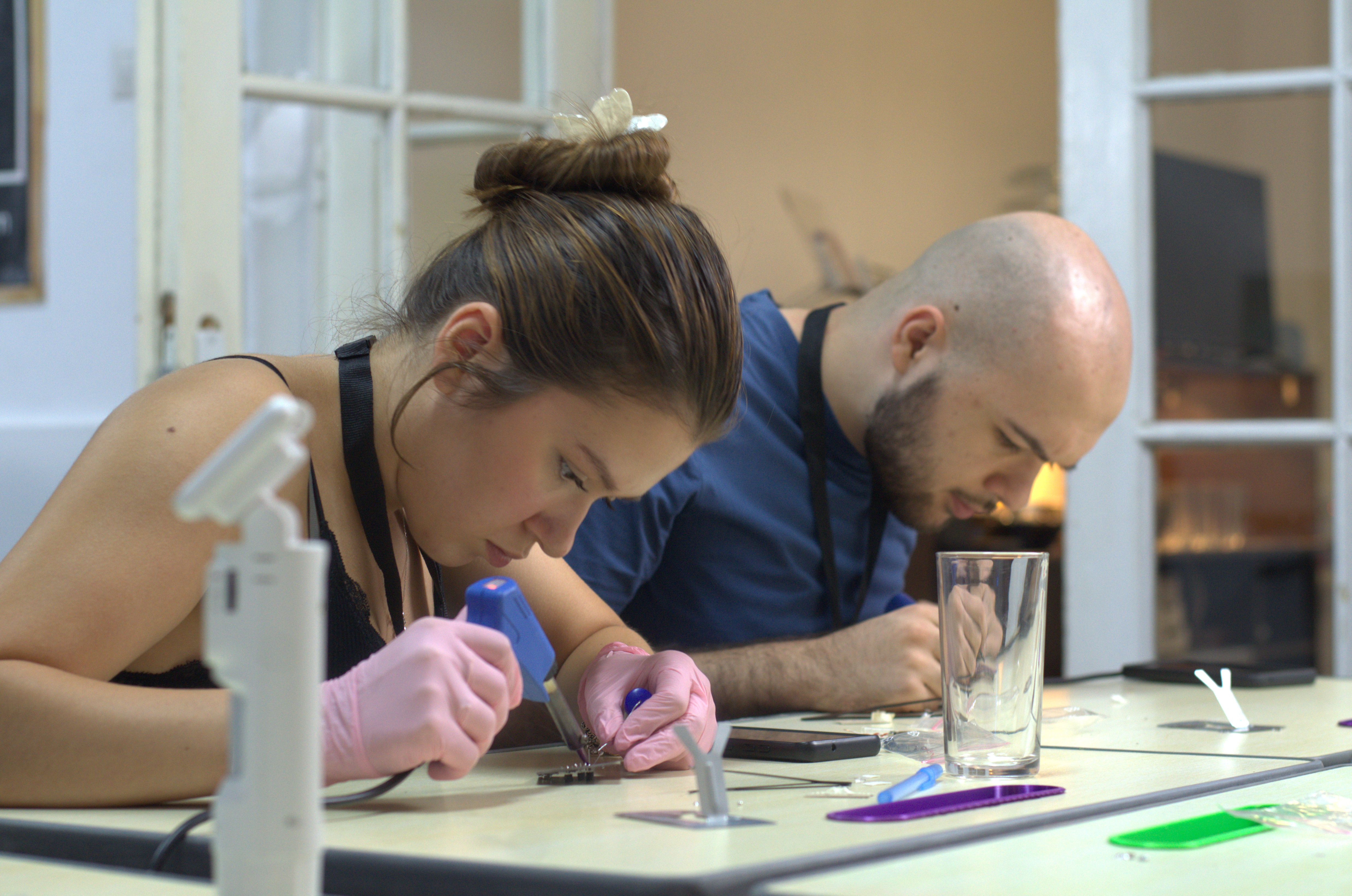 Two participants wearing gloves soldering components at a lab table