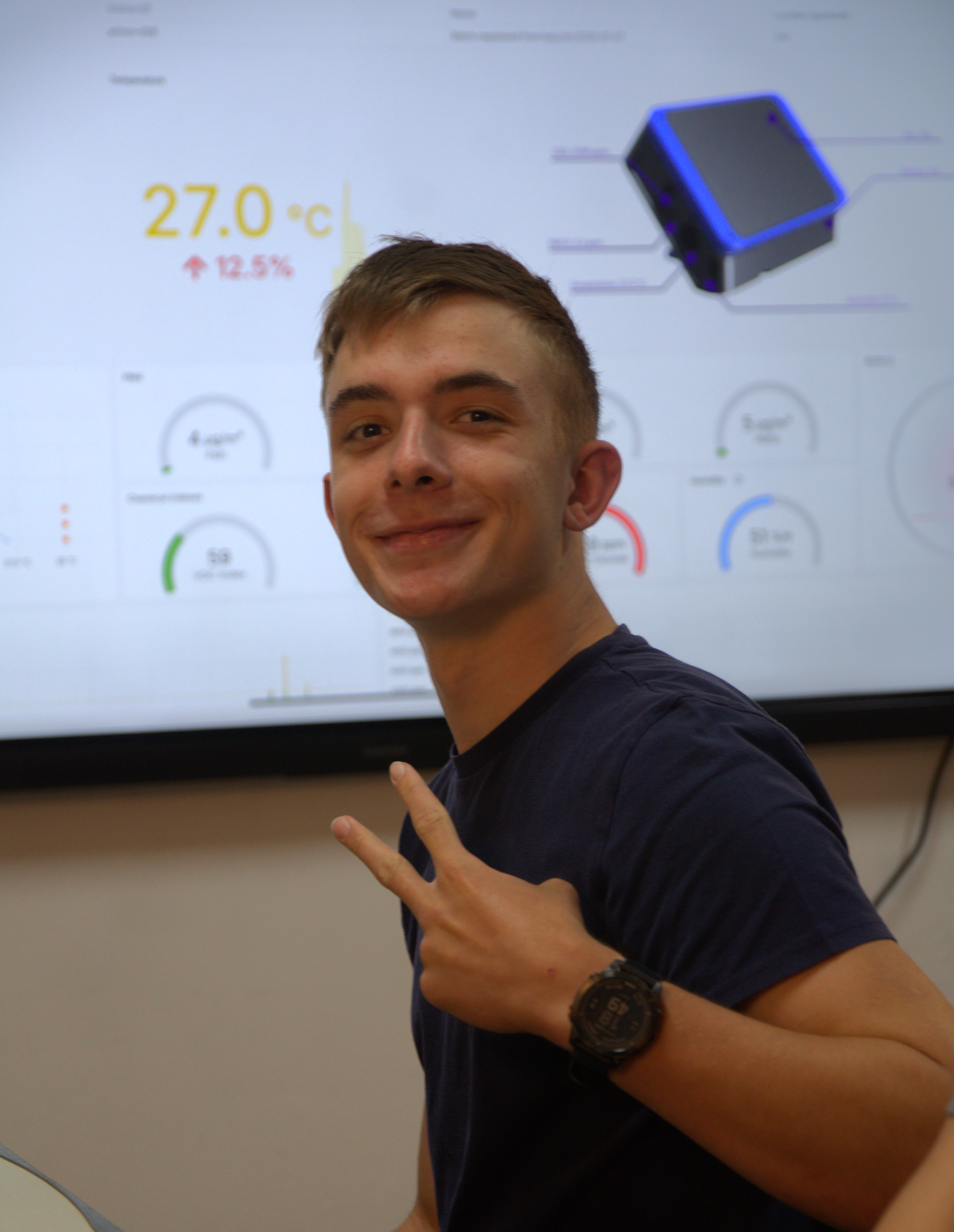 Smiling student making a peace sign in front of a screen showing AirBox data