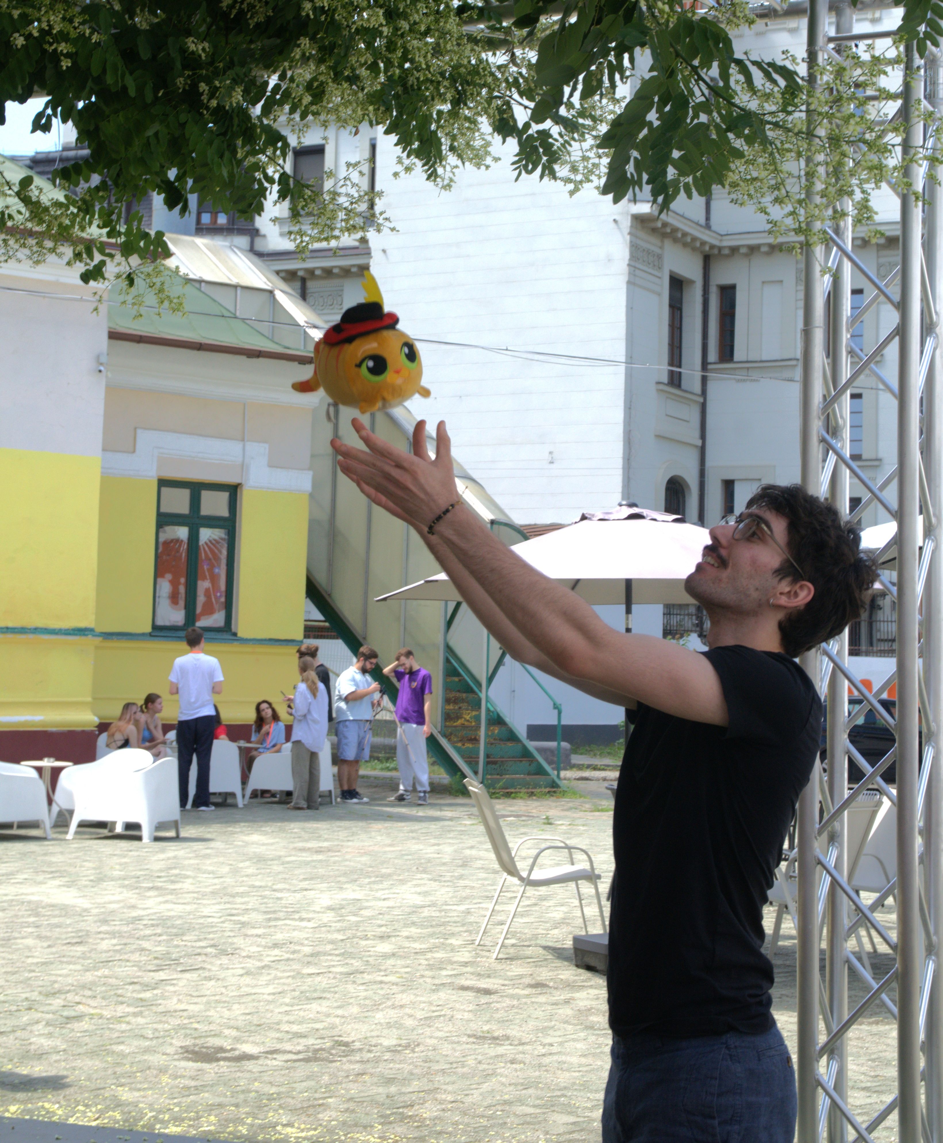 Student reaching up to catch a plush mascot in an outdoor courtyard