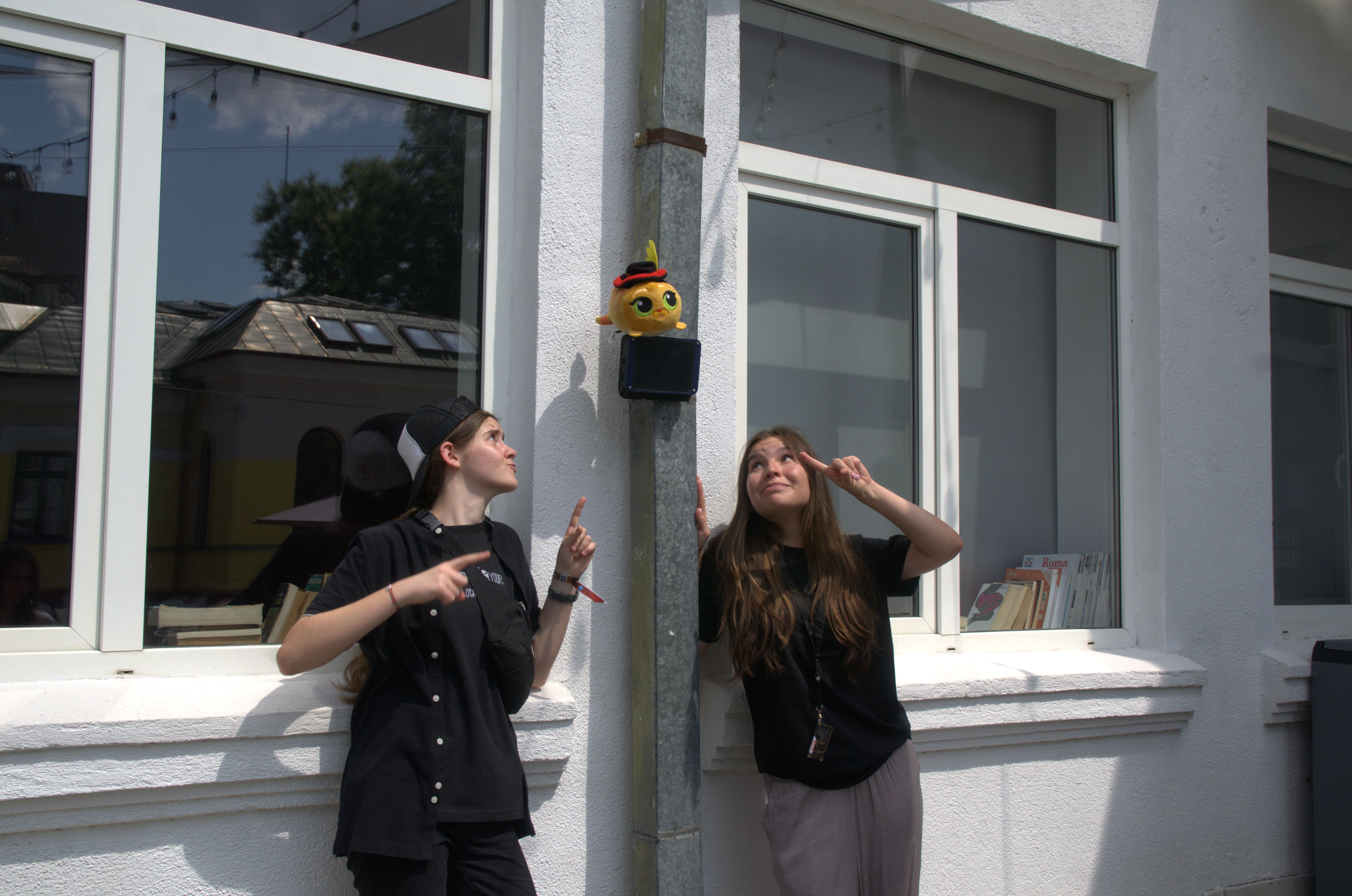 Two students pointing at an AirBox station mounted on a building wall outdoors