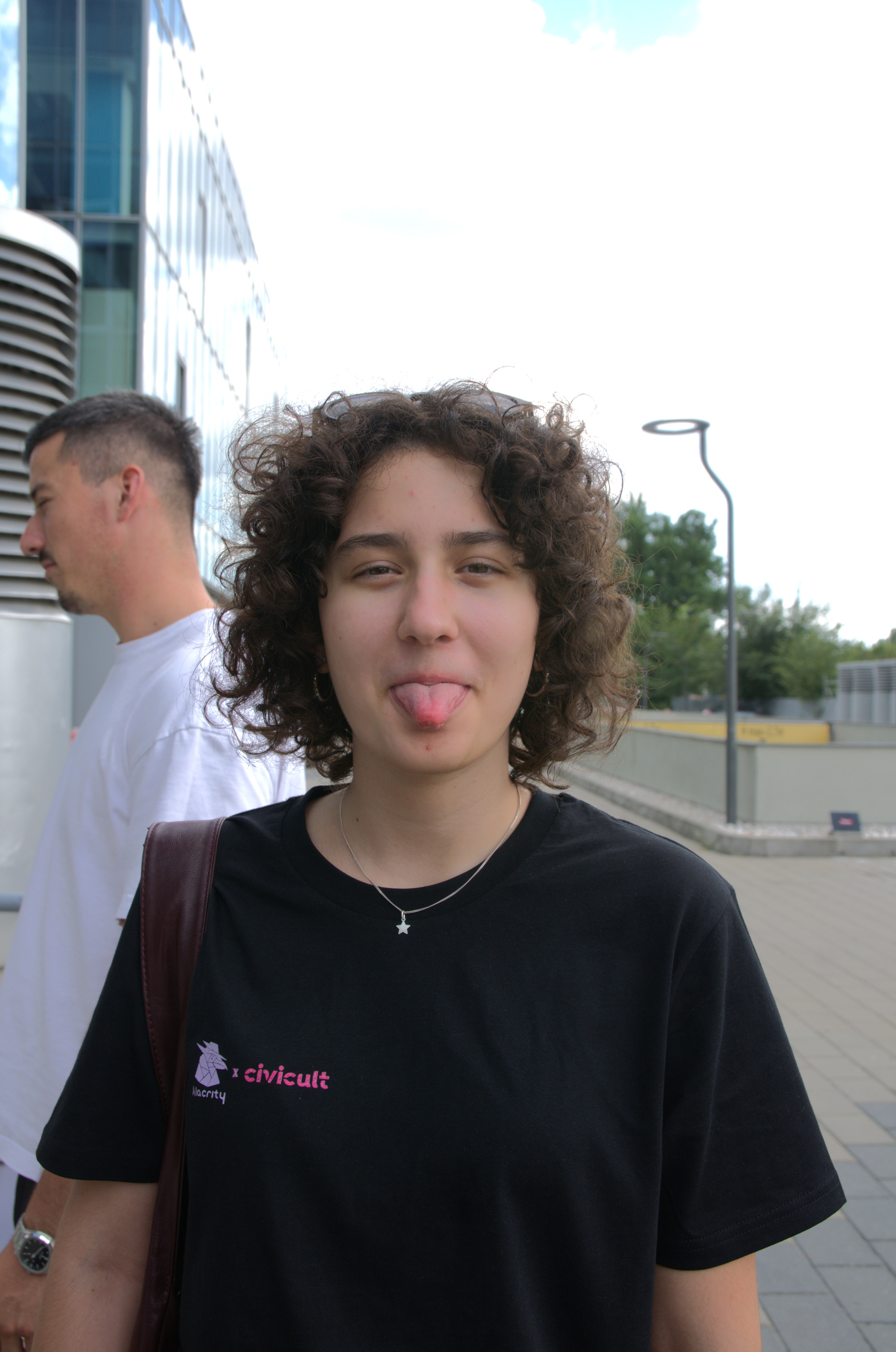 Student with curly hair sticking out their tongue outdoors