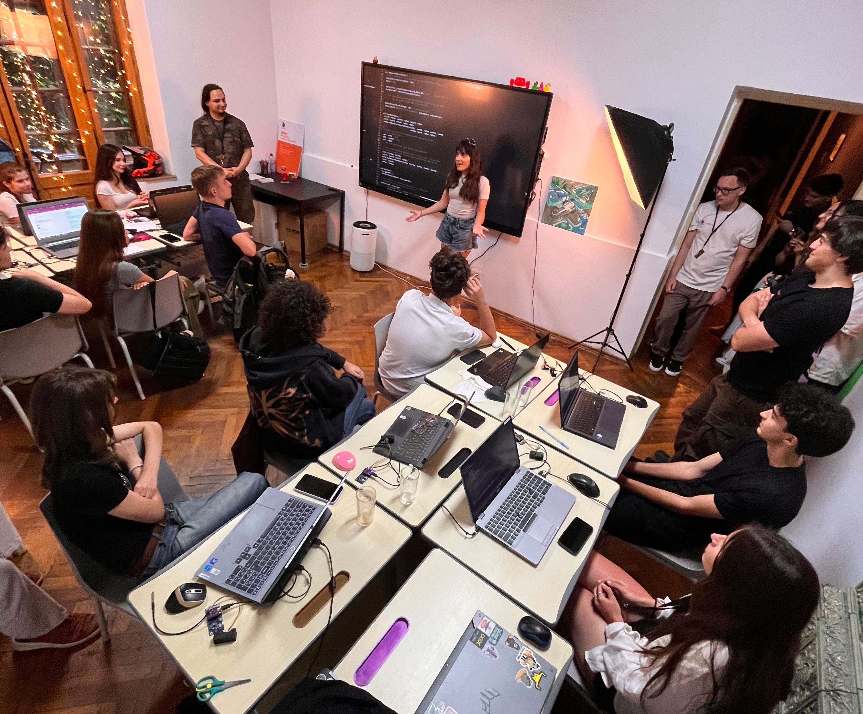 Overhead view of a class with students at laptops listening to a presenter in front of a screen